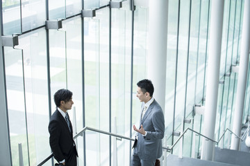Two businessmen have a stand talking in the lobby of the building
