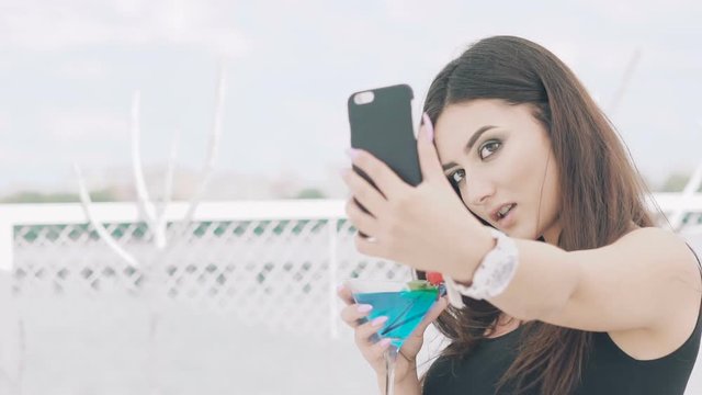 Young girl taking selfie with goblet of blue cocktail on the beach