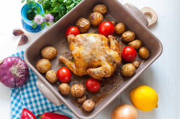 Roasted chicken with potato and tomato in ceramic dish, top view