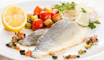 Baked fish with vegetables and lemon. On a white plate