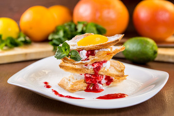 Dessert from flaky pastry with whipped cream and strawberry sauce. On a white plate and wooden table