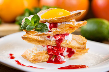 Dessert from flaky pastry with whipped cream and strawberry sauce. On a white plate