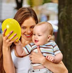 Fototapeta na wymiar Happy mother and her baby play with balloon outdoors in park. Baby keeps balloon. First baby birthday.