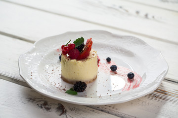 Small cake on plate. Dessert with berries. Cheesecake prepared at restaurant. Sweet dish of cottage cheese.