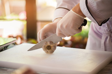 Hand with knife cuts garlic. Vegetable on white cooking board. Need a special ingredient. Chef...