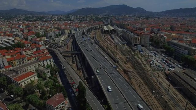 4K Nice city highway road traffic France aerial view from above. Fly over multiple lane motorway and train station in Nice Europe urban landscape with mountains background. Busy big city life concept