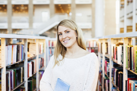 Portrait of beautiful university student standing in library