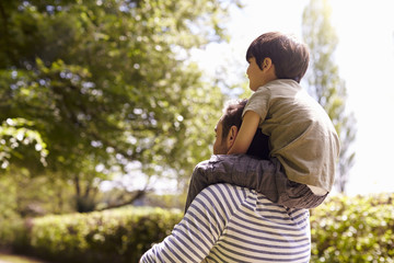 Rear View Of Father Giving Son Ride On Shoulders During Walk