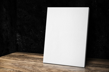 Blank white canvas frame leaning at grunge black stone wall and