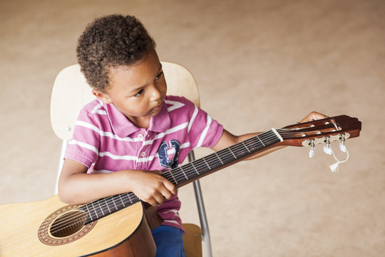 High angle view of boy playing guitar while sitting on chair