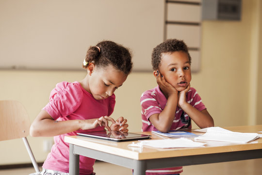 Girl using tablet computer while sitting by classmate in classroom