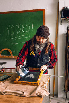Mature male worker pouring ink on screen printing frame at workshop