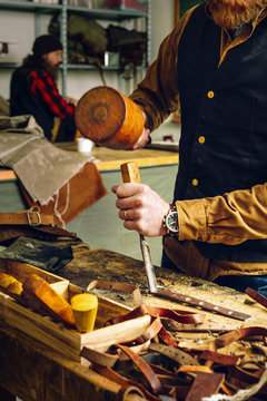 Midsection of worker using mallet and chisel to cut belt in workshop