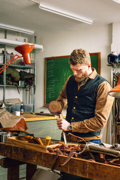 Man using mallet and chisel to cut belt in workshop