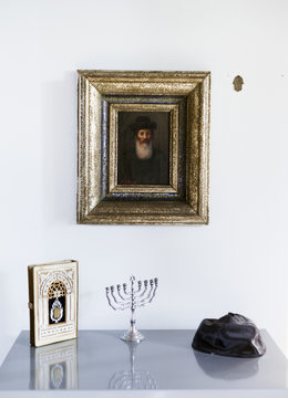 Picture frame above menorah, holy book and cap on table