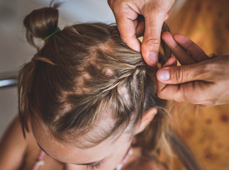 Mother is making of braids on little daughter's head.