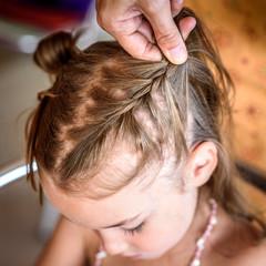 Naklejka premium Mother is making of braids on little daughter's head.