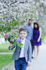Fototapeta premium The boy goes with the bouquet of lilacs blooming along the alley, in the background are embracing his parents, the look in the picture.