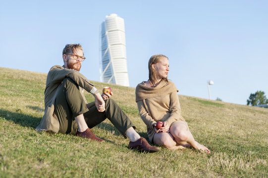 Low angle view of couple eating apples on grassy hill against Turing Torso