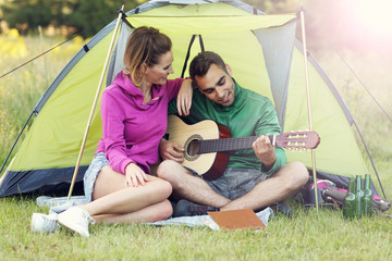 Couple camping in forest and playing guitar