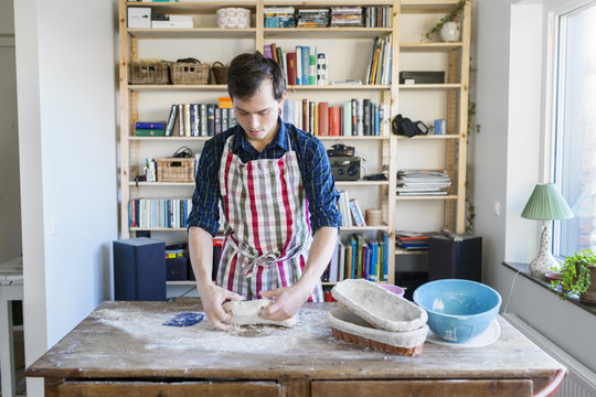 Baker kneading dough at table in bakery