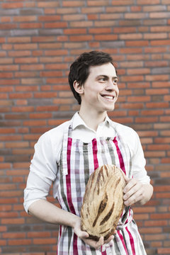 Baker holding bread loaves against brick wall