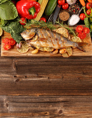 Grilled fish with vegetables on old wooden background with space