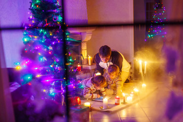 Young father and his little children sitting by a fireplace on C