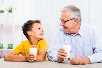 Grandfather and grandson are drinking milk at home. Healthy lifestyle.