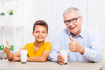 Grandfather and grandson are drinking milk at home. Healthy lifestyle.