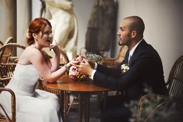 Bride tells something to a bald-headed groom sitting at the cafe