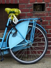 Blaues Damenrad und Hollandrad mit Mantelschoner und improvisiertem gelben Sattelschoner vor...