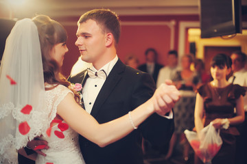 Gorgeous wedding couple dances in the shower of red petals