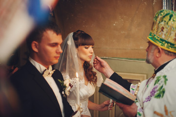 Priest reaches a wedding ring to bride's lips