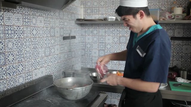 Kitchen worker puts the meat in the pot.