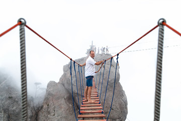 Человек проходит по подвесному мосту на скалах в тумане