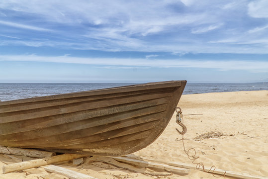 Old wooden fishing boat on beach. Blue sky with white clouds. Sunny day