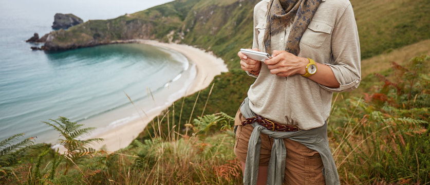 happy woman hiker writing sms in front of ocean view landscape