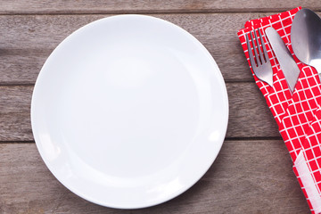 Top view of an empty white plate and cutlery in a red napkin on
