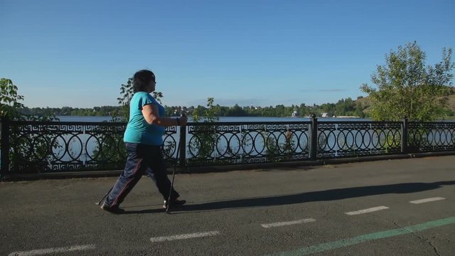 A woman walks through the Park with sticks for Nordic walking Sunny summer morning.