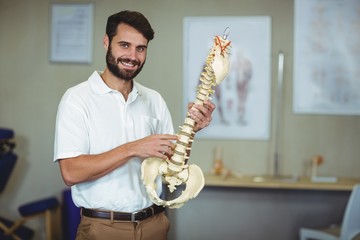 Male therapist holding spine model in clinic