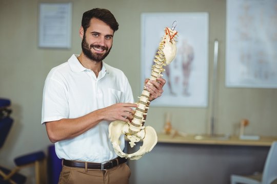 Male therapist holding spine model in clinic - Powered by Adobe