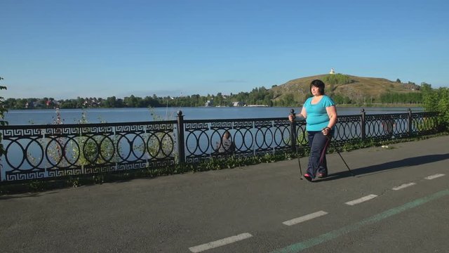 A woman walks through the Park with sticks for Nordic walking Sunny summer morning.