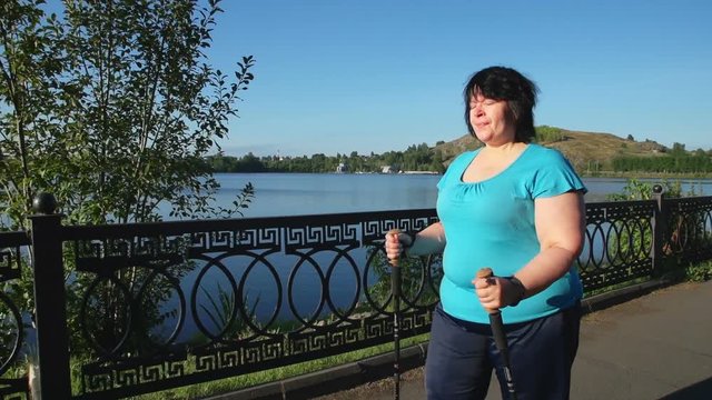 A woman walks through the Park with sticks for Nordic walking Sunny summer morning.
