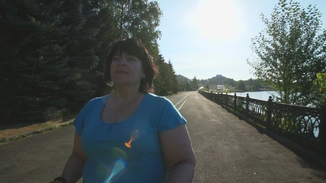 A woman walks through the Park with sticks for Nordic walking Sunny summer morning.
