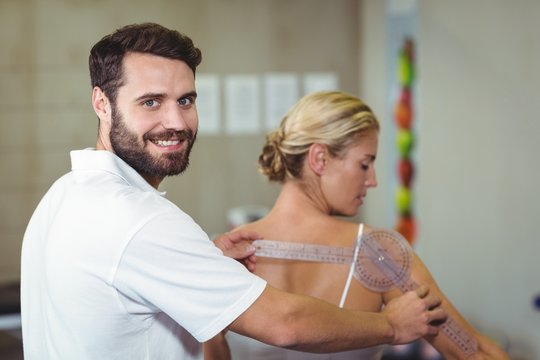 Male therapist measuring female patient back with goniometer