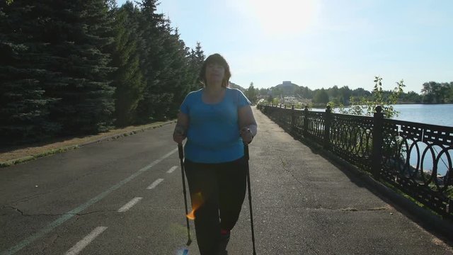 A woman walks through the Park with sticks for Nordic walking Sunny summer morning.