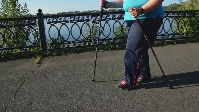 A woman walks through the Park with sticks for Nordic walking Sunny summer morning.