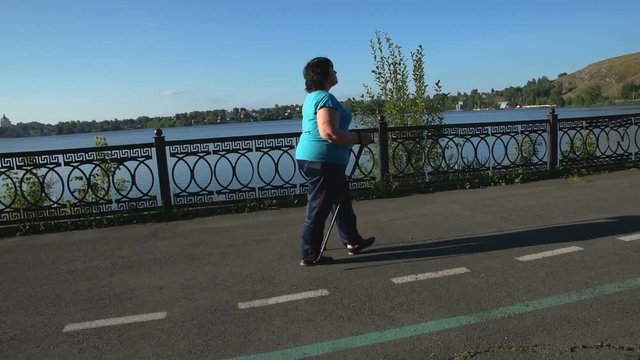 A woman walks through the Park with sticks for Nordic walking Sunny summer morning.