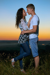 romantic couple embrace at sunset, beautiful landscape and bright yellow sky, love tenderness concept, young adult people